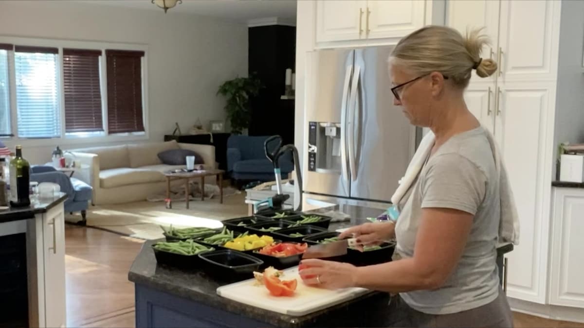 Kristin chopping peppers at her kitchen island beside trays of prepped meals